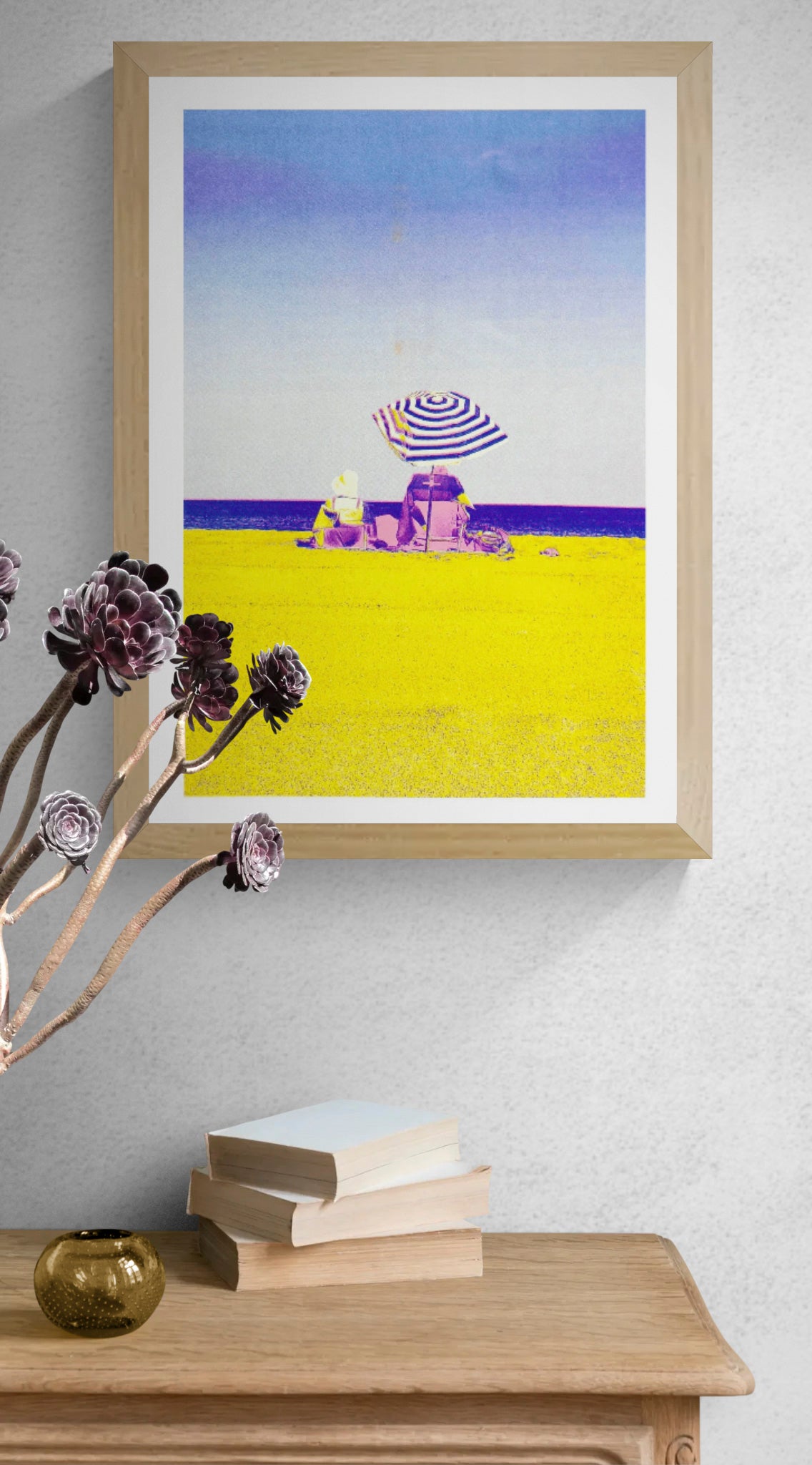 Colorful risograph art print titled “Basque Beach” by PTRVRKD, featuring two people sitting under a striped umbrella on a bright yellow beach with a soft blue-purple sky; A3 limited edition printed on Munken Pure Rough paper. Vibrant modern beach artwork ideal for coastal decor and contemporary wall art collectors.