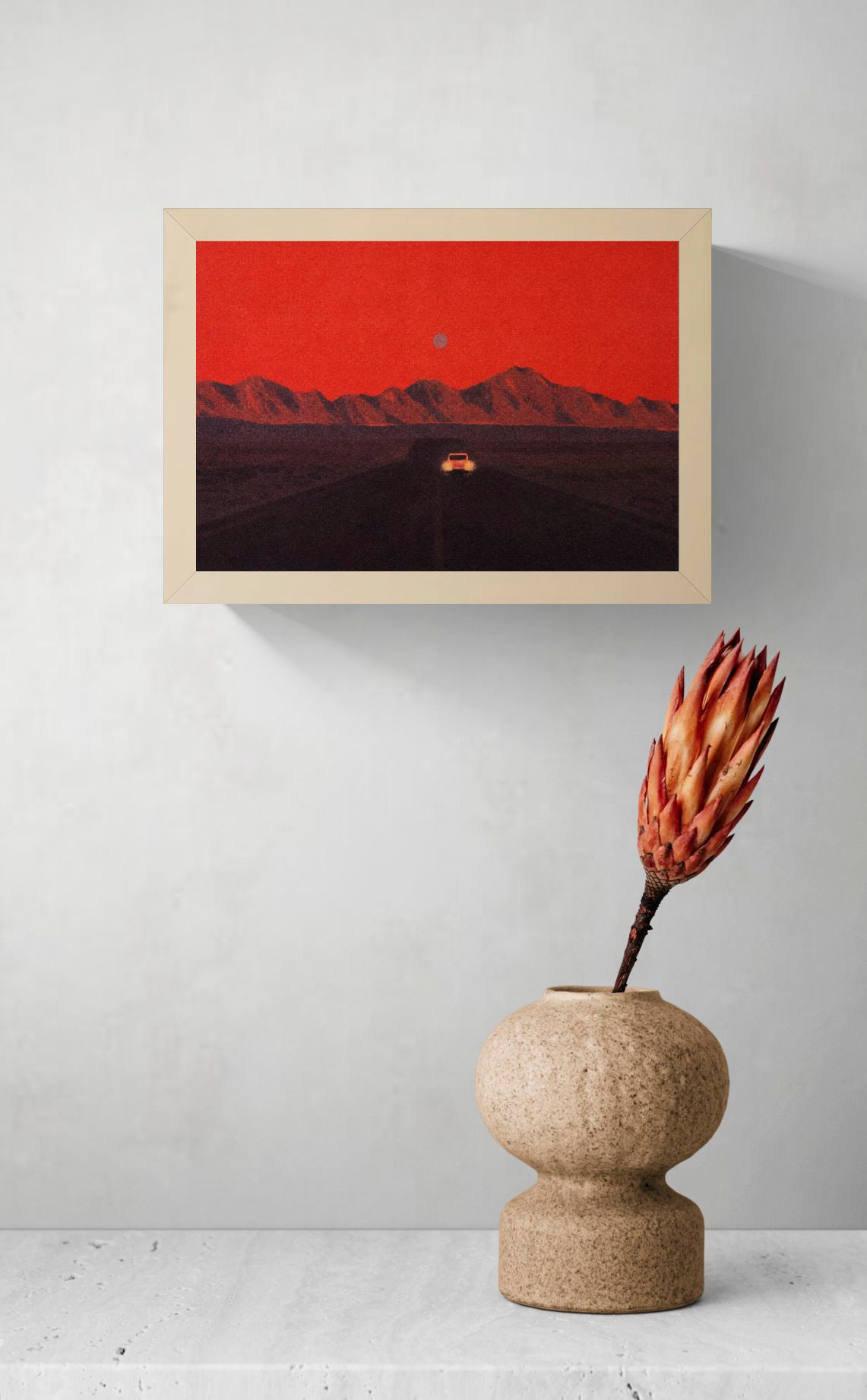 Namibia by Linde Raats, horizontal A6 giclée print showing a car driving toward dark mountains beneath a textured red sky, atmospheric wall art for modern home decor.