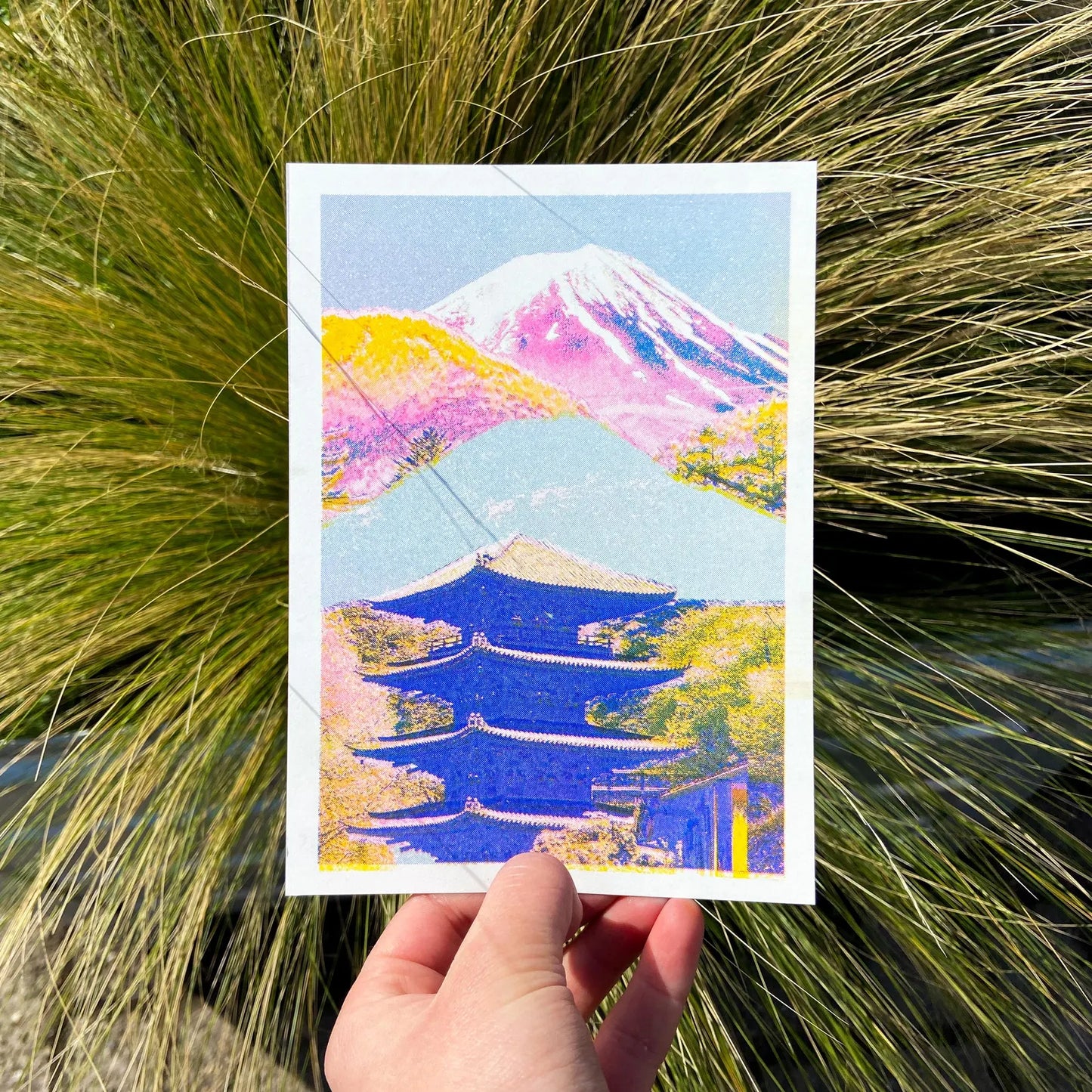 Colorful risograph art print of a Japanese landscape by PTRVRKD featuring Mount Fuji in soft pink and purple tones, a blue traditional pagoda, and vibrant yellow-orange trees. Modern Japanese collage illustration, handprinted with soy inks on high-quality Biotop paper. Perfect for Japan lovers and contemporary design enthusiasts.