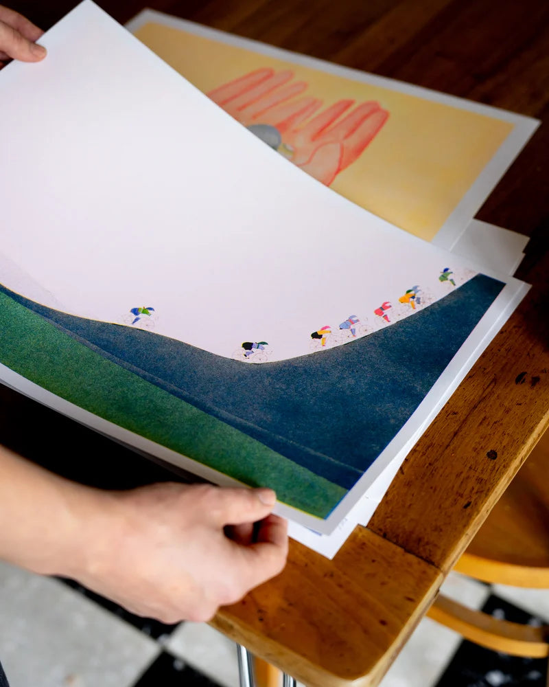 Four-color risograph art print La montée by Viola Amman showing colorful cyclists climbing a steep green hill against a pale background. Minimalist, playful wall art full of motion and optimism, ideal for cycling lovers and modern interiors.