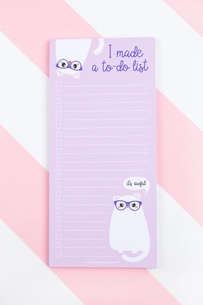 Funny to-do notepad in soft lilac featuring a white cartoon cat with glasses and a sarcastic speech bubble that says "it's awful", perfect for list lovers who appreciate humor – designed by Studio Inktvis in the Netherlands.