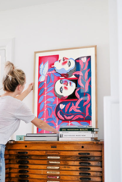 Bonding by Carla Petelski, contemporary figurative digital art print featuring two stylized faces surrounded by pink and blue botanical forms, modern emotional wall art in vibrant colors