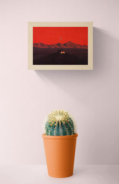 Namibia by Linde Raats, horizontal A6 giclée print showing a car driving toward dark mountains beneath a textured red sky, atmospheric wall art for modern home decor.