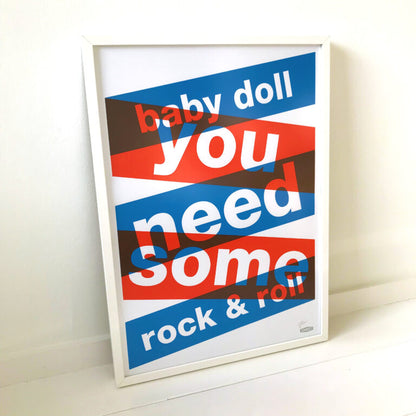 Three-color screen print ‘BABYDOLL’ by Dutch duo Gumbootz, featuring bold overlapping red, blue and grey text saying ‘baby doll you need some rock & roll,’ arranged in dynamic angled blocks on a 50×70 cm art poster; modern graphic typography artwork perfect for contemporary interiors.