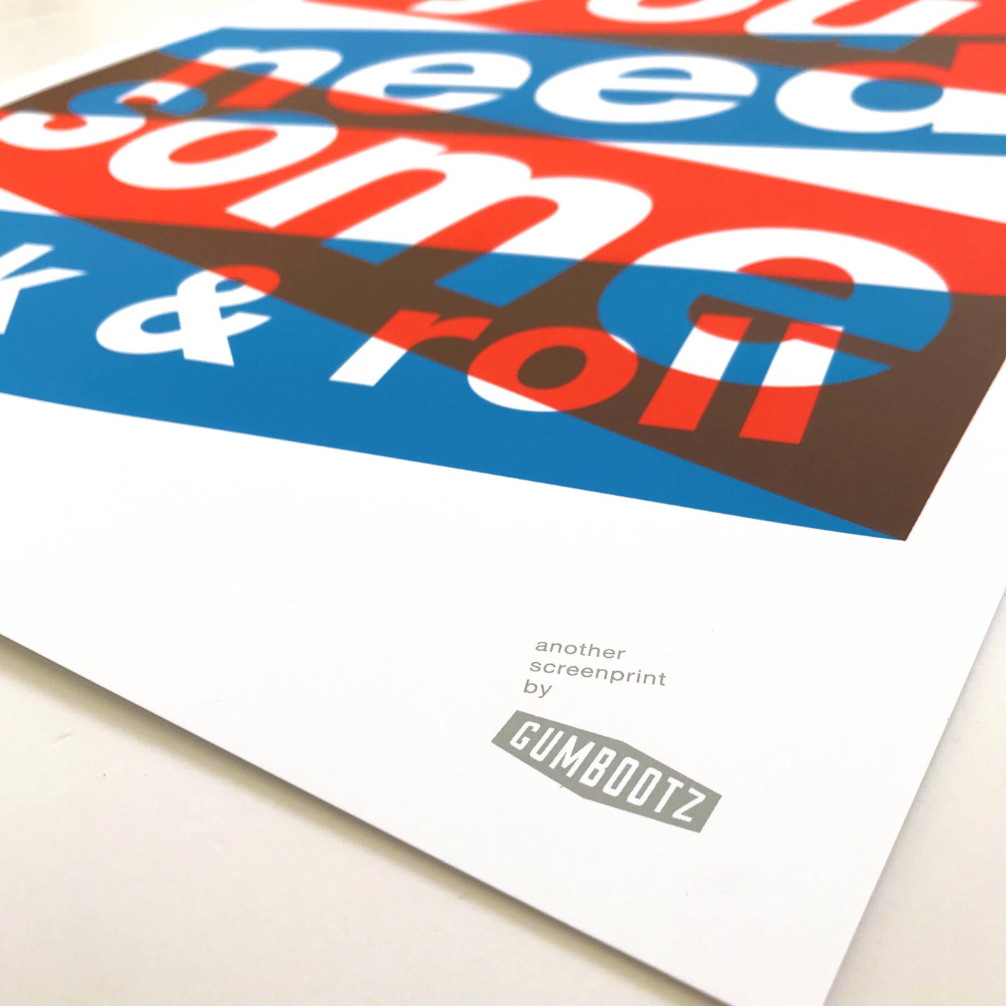 Three-color screen print ‘BABYDOLL’ by Dutch duo Gumbootz, featuring bold overlapping red, blue and grey text saying ‘baby doll you need some rock & roll,’ arranged in dynamic angled blocks on a 50×70 cm art poster; modern graphic typography artwork perfect for contemporary interiors.