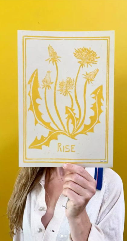 Handmade yellow linocut art print by Belgian artist Leda Vaes titled “Rise,” featuring stylized dandelion flowers and leaves carved in a bold, organic design; A4 nature-inspired print with warm, uplifting botanical energy.