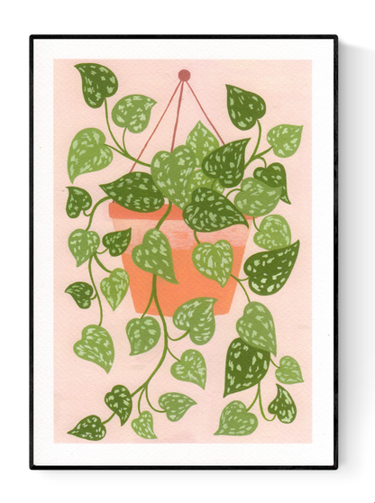 Digital art print titled “Scindapsus” by Belgian illustrator Leens, featuring a lush cascading houseplant with heart-shaped green leaves in a terracotta hanging pot, against a soft pink background. Printed on A4 fine art paper.