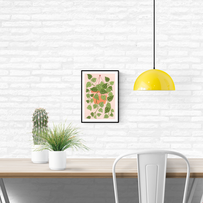 Digital art print titled “Scindapsus” by Belgian illustrator Leens, featuring a lush cascading houseplant with heart-shaped green leaves in a terracotta hanging pot, against a soft pink background. Printed on A4 fine art paper.