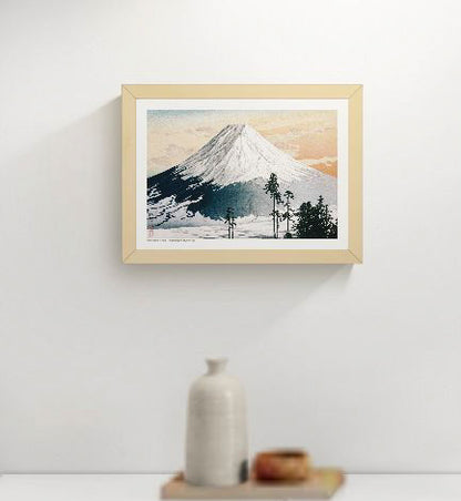 Landscape A4 art print of snow-covered Mount Fuji beneath a peach and blue sky, with dark pine trees in the foreground, based on a Japanese colour woodblock by Hiroaki Takahashi; horizontal wall art for calm interiors.