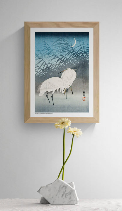 Two white egrets standing among layered reeds beneath a crescent moon, illustrated in a vintage Japanese woodblock style with blue and grey tones, vertical A4 digital print for calm wall decor.
