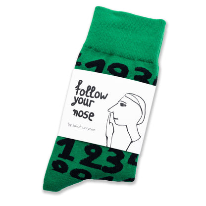 Green crew socks with playful black numbers by Sarah Corynen – unisex cotton blend, size 38-42, bold and quirky design for math fans and creative wardrobes.
