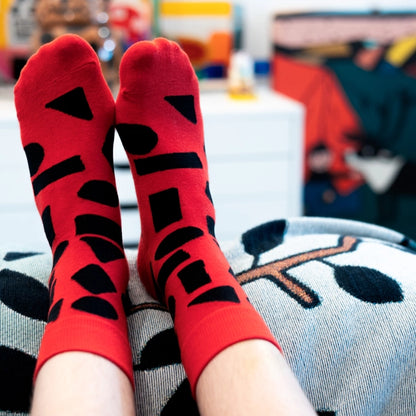 Red crew socks with bold black abstract shapes by Sarah Corynen – size 38-42 unisex cotton blend, playful geometric design for creative and colorful style.