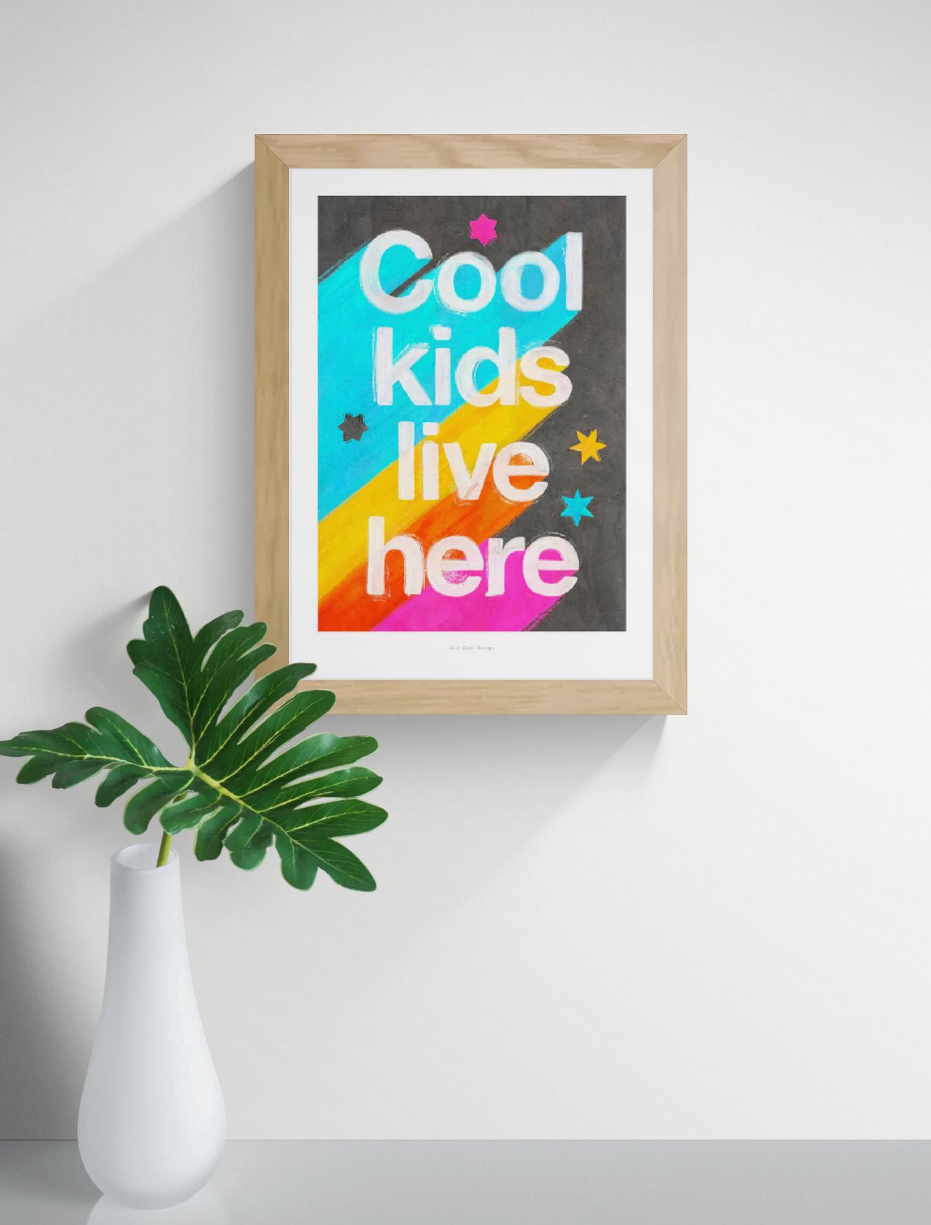 Giclée art print by Just Cool Design with the phrase "Cool kids live here" in bold white letters over a bright rainbow background with stars, ideal for colorful children's rooms or playful modern decor.