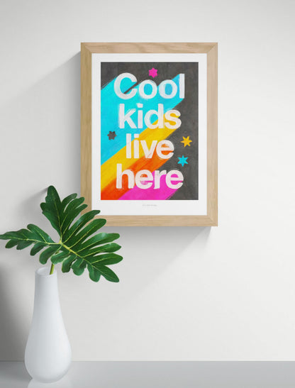 Giclée art print by Just Cool Design with the phrase "Cool kids live here" in bold white letters over a bright rainbow background with stars, ideal for colorful children's rooms or playful modern decor.