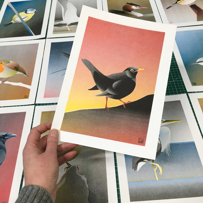 Blackbird illustration by VrijFormaat featuring a sleek black bird against a warm sunset gradient background — modern nature-inspired wall art available at Galerie Frits