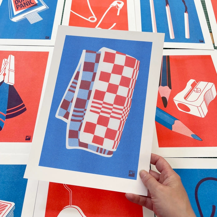 A4 risograph print titled Towel by Dutch studio VrijFormaat. Features a red and blue checkered dish towel illustrated in bold, minimalist style. Part of the “Extra Ordinary” series, printed on 160g Biotop paper using soy-based risography ink. Ideal for lovers of design, pattern, and printmaking.