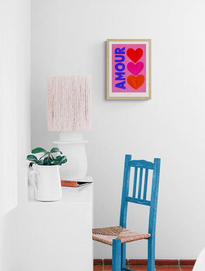 Bright pop art print with the word “AMOUR” in bold blue letters beside three colorful hearts (red, pink, and orange) on a pink background — Amour by Just Cool Design, vibrant Giclée art print for modern interiors and love-themed wall decor.