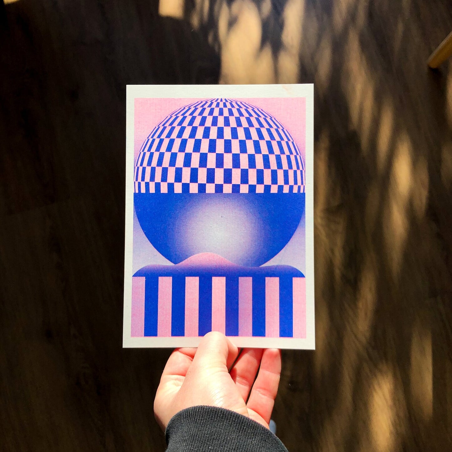 Pink and blue geometric risograph print by Dutch illustrator PTRVRKD – abstract optical landscape with checkerboard sphere, striped base, and dreamy gradient design, printed with eco-friendly soy inks on 250 gsm Biotop paper, handmade in the Netherlands – bold modern wall art for graphic design enthusiasts.