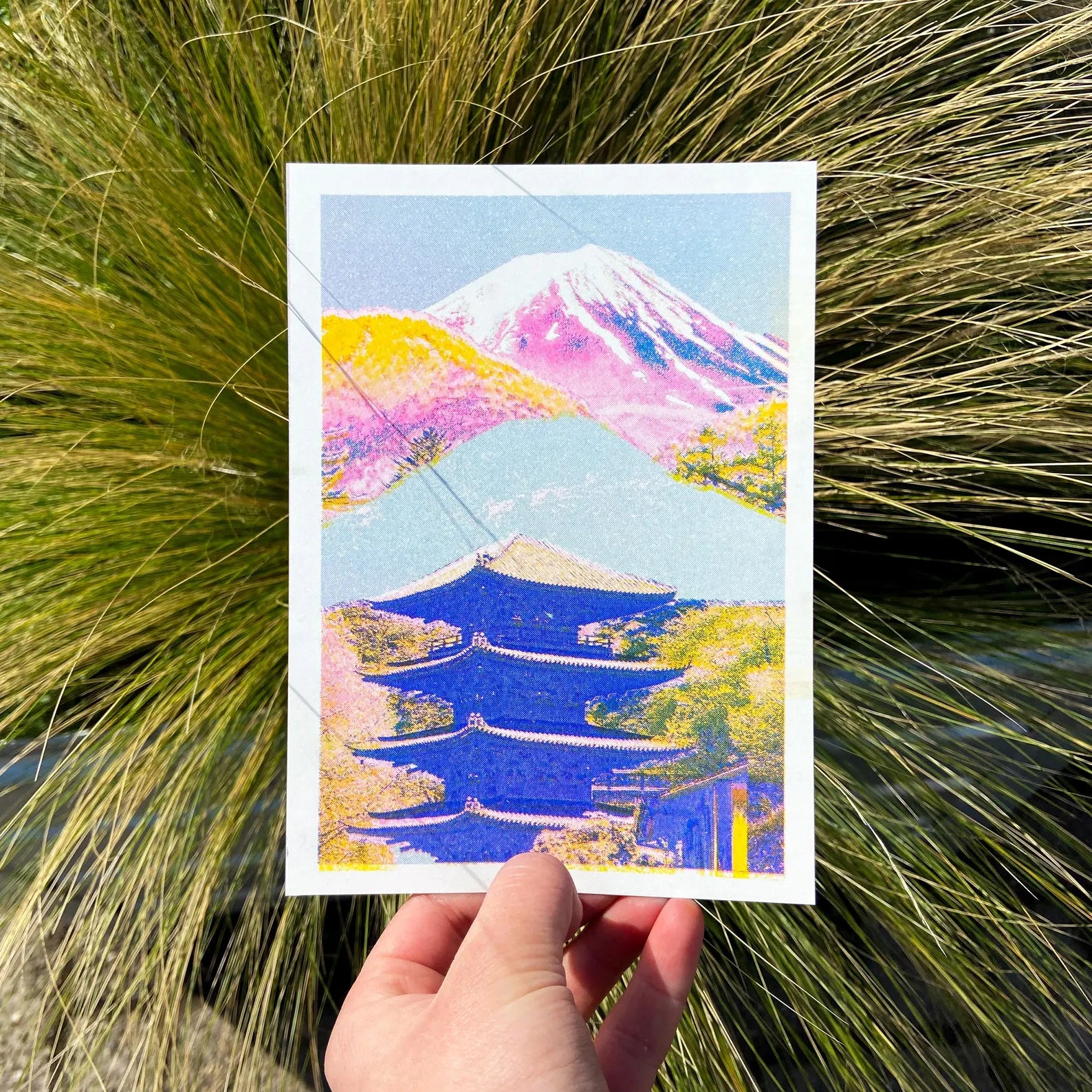 Colorful risograph art print of a Japanese landscape by PTRVRKD featuring Mount Fuji in soft pink and purple tones, a blue traditional pagoda, and vibrant yellow-orange trees. Modern Japanese collage illustration, handprinted with soy inks on high-quality Biotop paper. Perfect for Japan lovers and contemporary design enthusiasts.