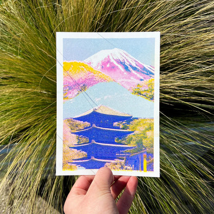 Colorful risograph art print of a Japanese landscape by PTRVRKD featuring Mount Fuji in soft pink and purple tones, a blue traditional pagoda, and vibrant yellow-orange trees. Modern Japanese collage illustration, handprinted with soy inks on high-quality Biotop paper. Perfect for Japan lovers and contemporary design enthusiasts.