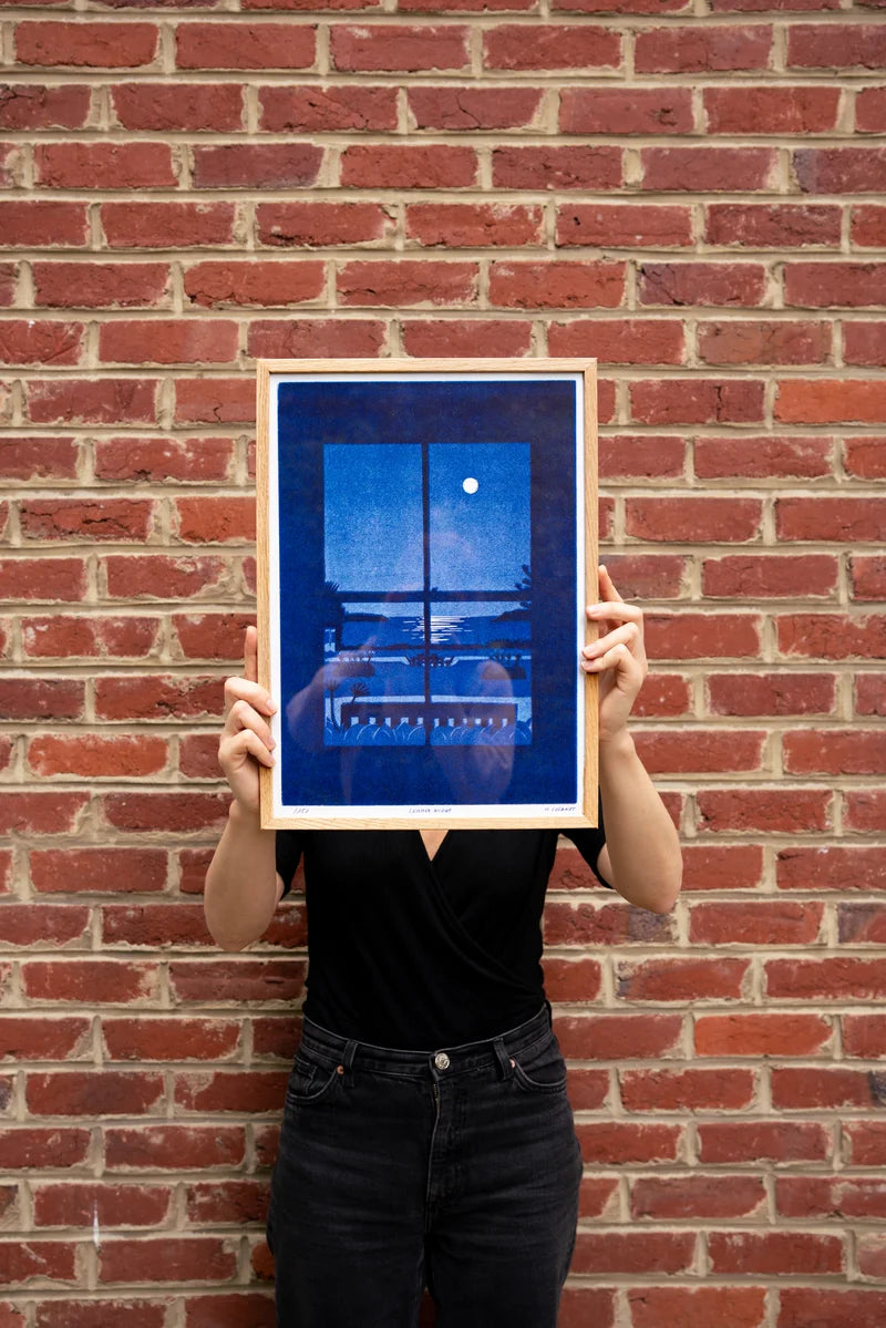 Summer Night by French illustrator Mathilde Solanet, A3 (29.7 x 42 cm) risograph print in 3 colors, limited edition of 150 signed and numbered copies. Artwork shows a serene moonlit coastal landscape through a window in rich blue tones. Printed on 150g Munken Print White paper, made in Belgium, unframed, packaged in protective sleeve with cardboard backing.