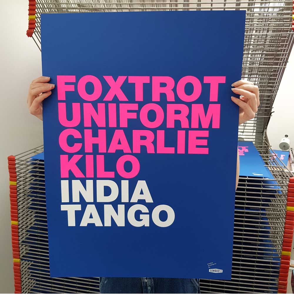 Large blue screen print with bold pink and white typography spelling 'Foxtrot Uniform Charlie Kilo India Tango' by Dutch artist Gumbootz — modern statement art poster, ideal for contemporary spaces.